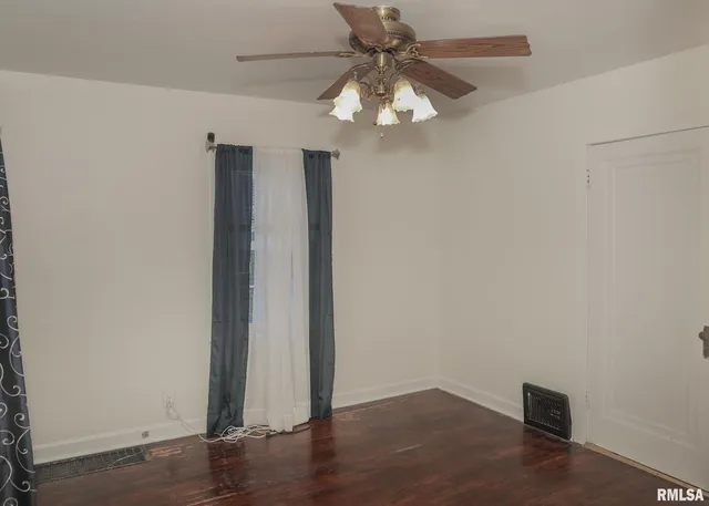 an empty room with wooden floor fan and windows
