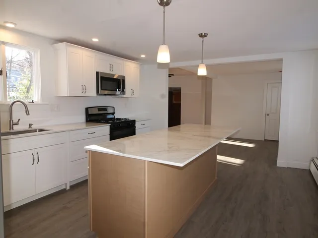 a kitchen with stainless steel appliances granite countertop a sink a microwave oven a refrigerator and white cabinets with wooden floor