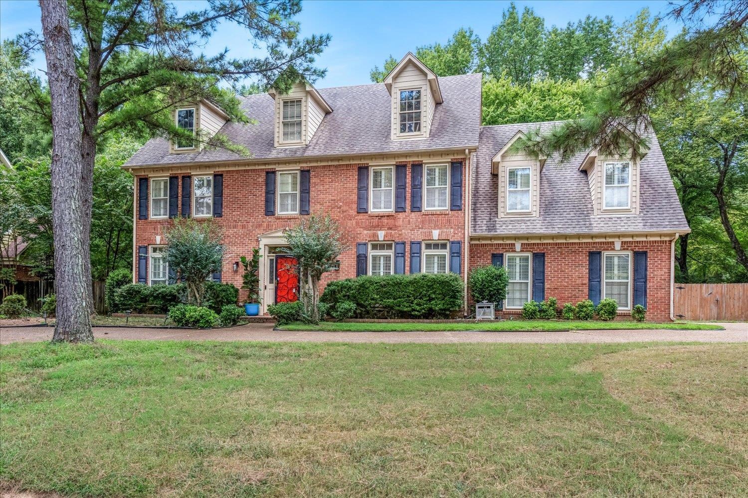 65 Summer Grove Road Memphis, TN 38018 - Photo 1 of 38 Brick exterior with dormer windows, complemented by a red front door, blue shutters, and mature landscaping
