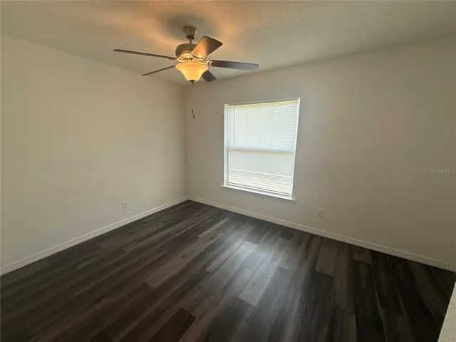 an empty room with wooden floor fan and windows
