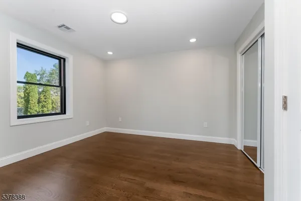 an empty room with wooden floor closet and windows