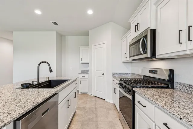a large kitchen with stainless steel appliances granite countertop a sink and dishwasher a stove top oven with white cabinets