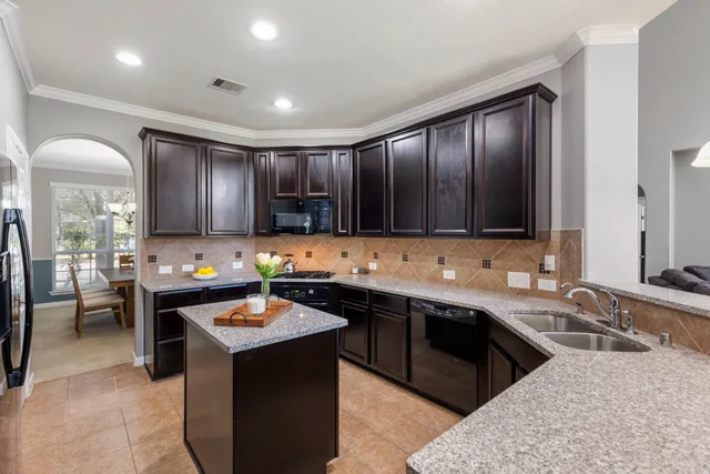 a kitchen with stainless steel appliances kitchen island granite countertop a sink dishwasher stove and refrigerator with wooden cabinet