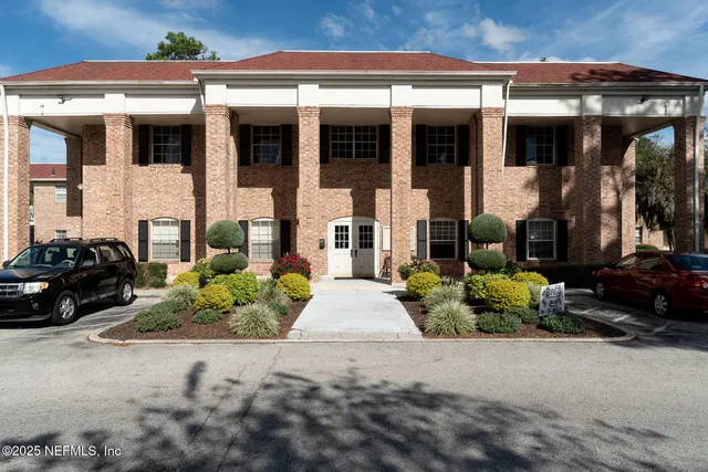 a view of a brick house with a yard plants and large tree