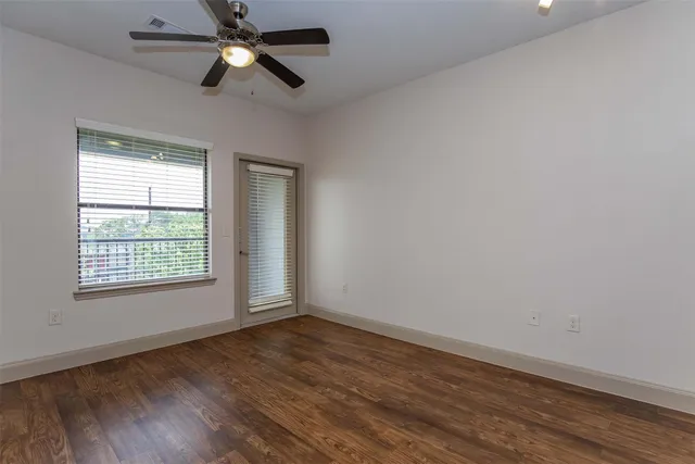 an empty room with wooden floor ceiling fan and windows