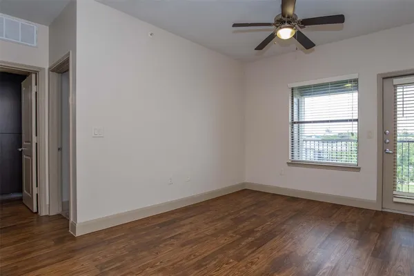 an empty room with wooden floor fan and windows