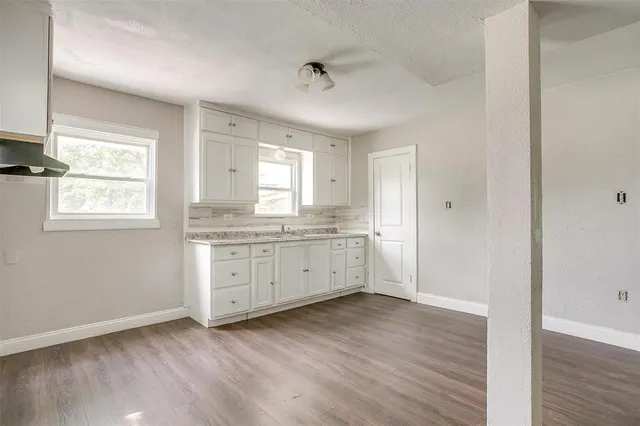 a room with kitchen island granite countertop white cabinets and wooden floor