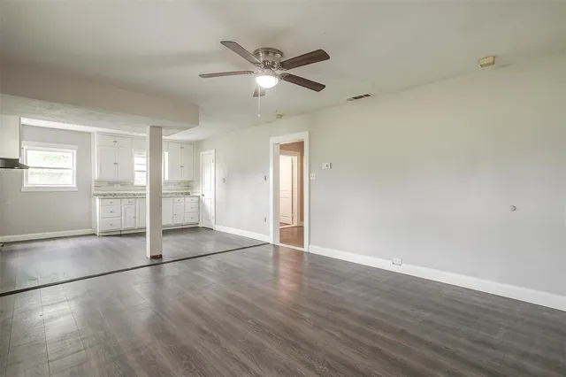 an empty room with wooden floor fan and windows