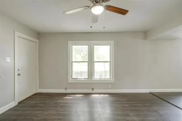 an empty room with wooden floor fan and windows
