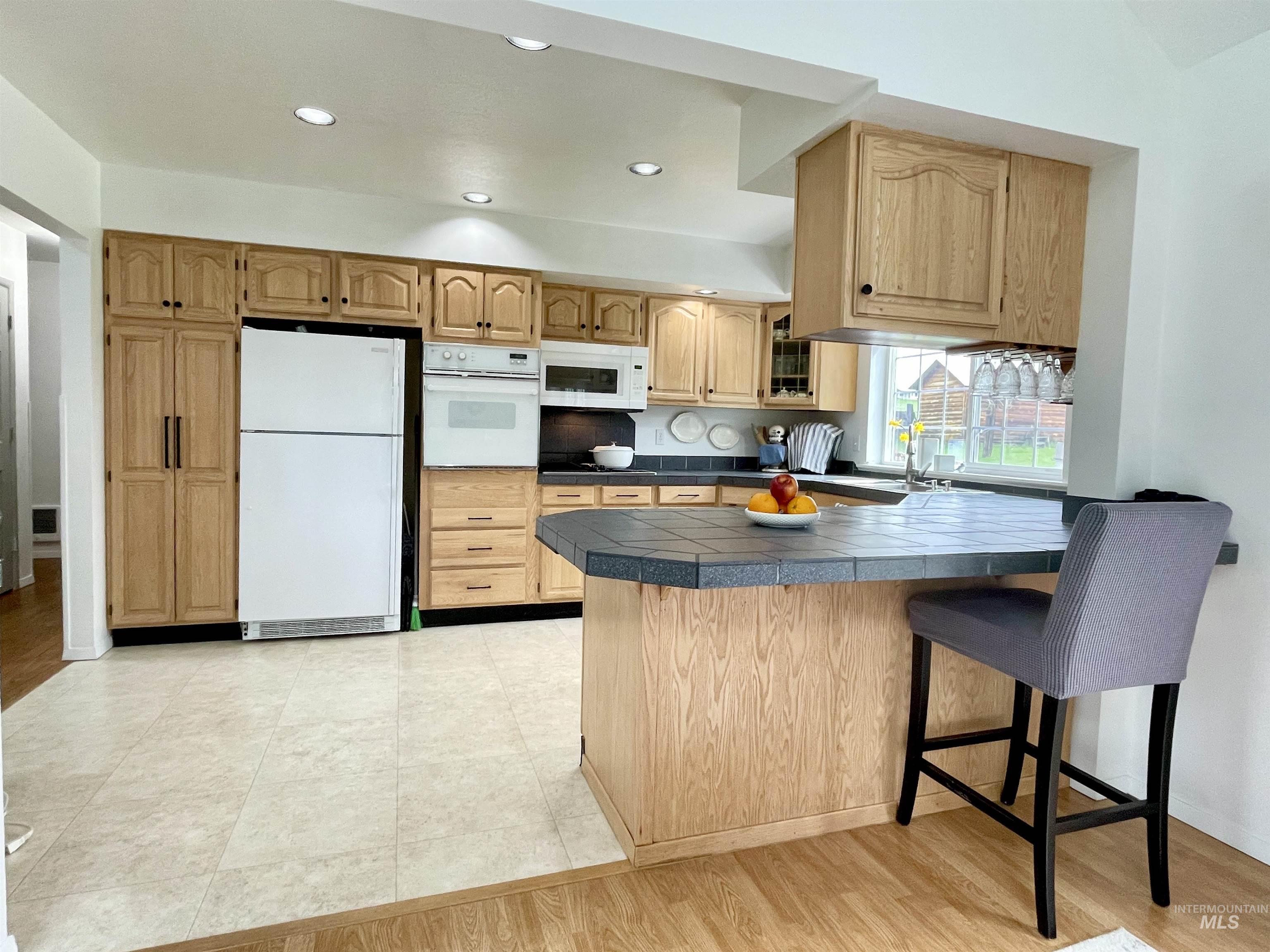637 Leitch Creek Road Kooskia, ID 83539 - Photo 14 of 38 Kitchen with a peninsula, white appliances, tile counters, a breakfast bar area, and light wood-style flooring