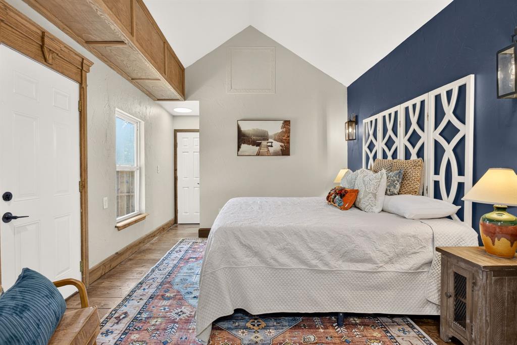 702 West Spring Street Weatherford, TX 76086 - Photo 37 of 39 Vaulted ceiling bedroom featuring a contrasting accent wall, decorative wood-finish trim, a high transom window, and a built-in overhead storage shelf