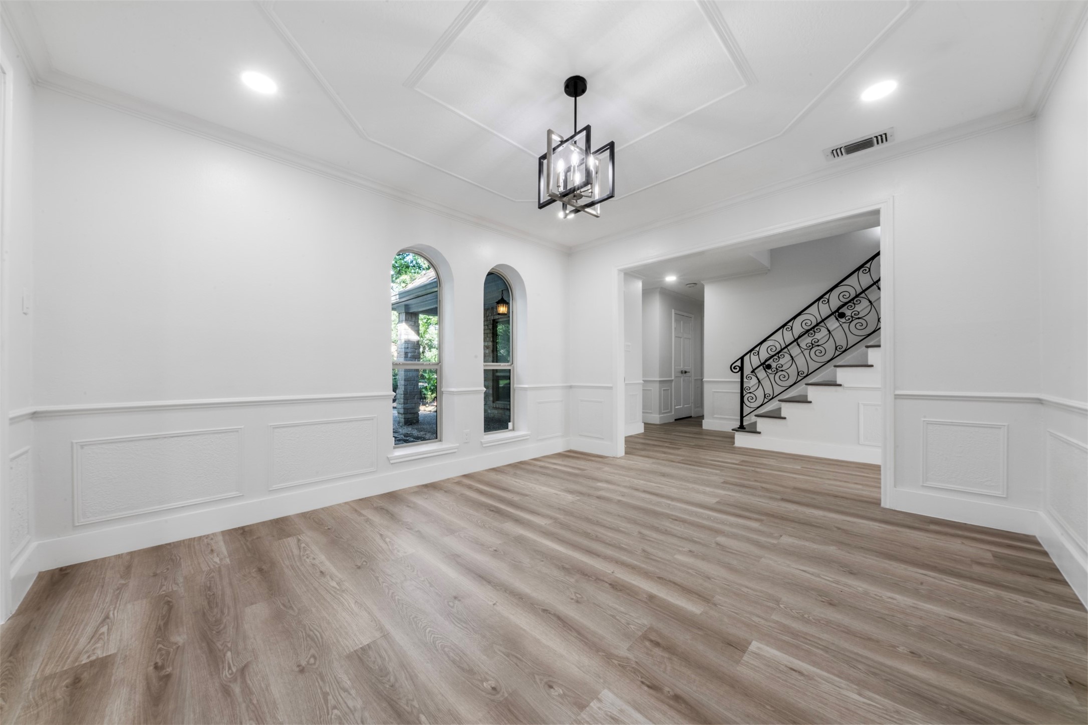 9543 Enstone Circle Spring, TX 77379 - Photo 12 of 50 This photo showcases a bright, open room with modern wood flooring and elegant wainscoting. It features two arched windows, a stylish ceiling light fixture, and a decorative staircase with ornate railing, creating a sophisticated entry or living space.