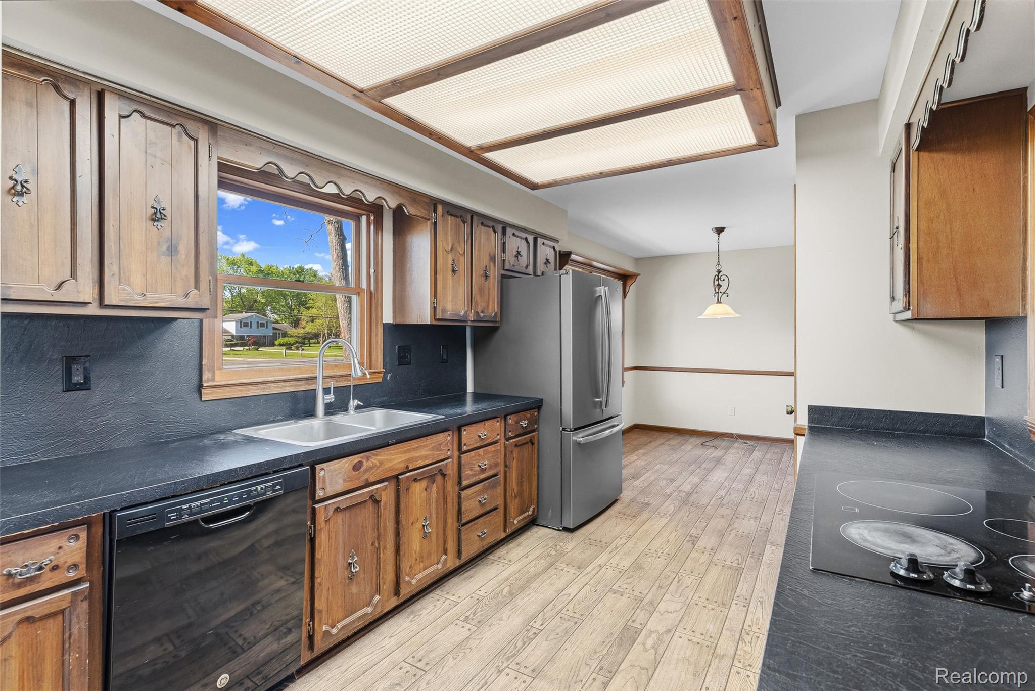 4191 McCandlish Road Grand Blanc, MI 48439 - Photo 22 of 53 Kitchen featuring dark countertops, decorative light fixtures, black appliances, light wood-style floors, and wood finish cabinetry