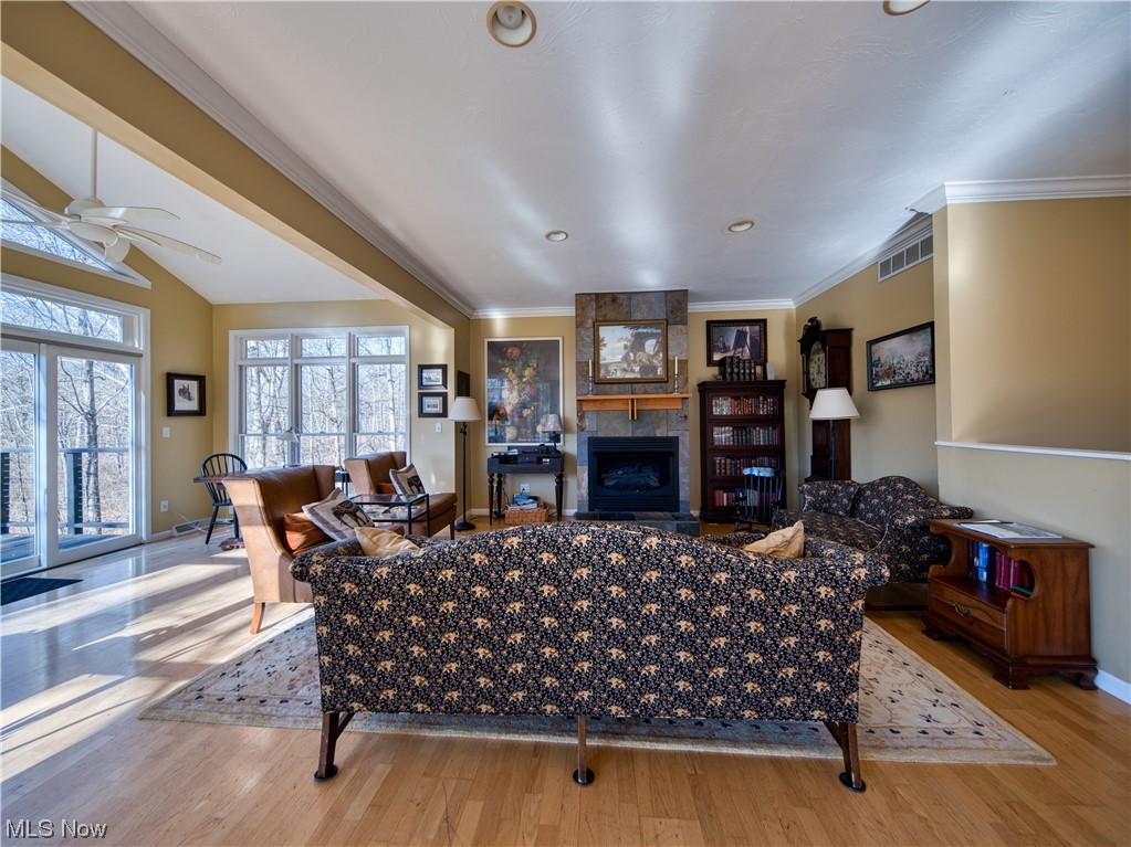 Living room with vaulted ceiling, light hardwood / wood-style floors, ceiling fan, ornamental molding, and a tiled fireplace