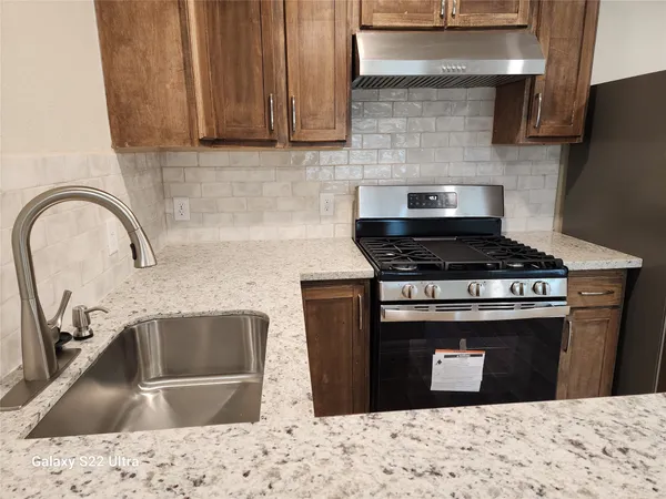 a kitchen with granite countertop a stove and a sink with wooden cabinets