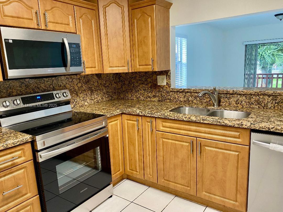 11287 Southwest 88th Street, Unit 209L Miami, FL 33173 - Photo 7 of 16 a kitchen with granite countertop a stove top oven cabinetry a sink and a window