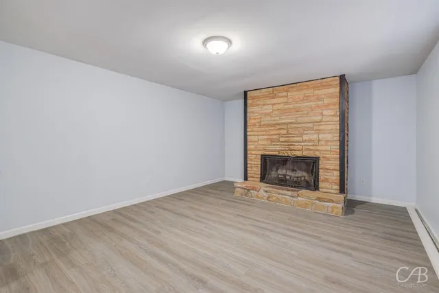 a view of an empty room with wooden floor fireplace and a window