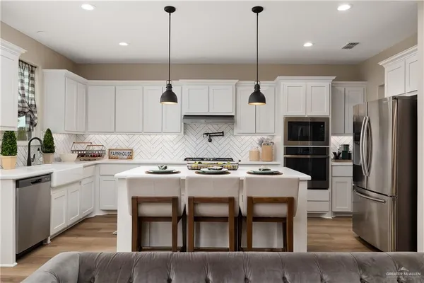 a kitchen with kitchen island a stove a refrigerator a sink a oven and white cabinets with wooden floor