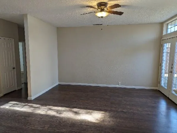 an empty room with wooden floor fan and windows