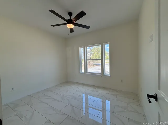 an empty room with ceiling fan and windows