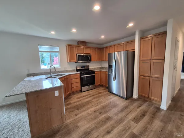 a kitchen with stainless steel appliances granite countertop a refrigerator a sink a stove a microwave and island with wooden floor