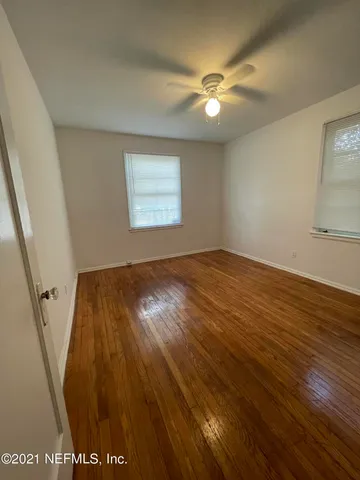 a view of an empty room with wooden floor and a ceiling fan
