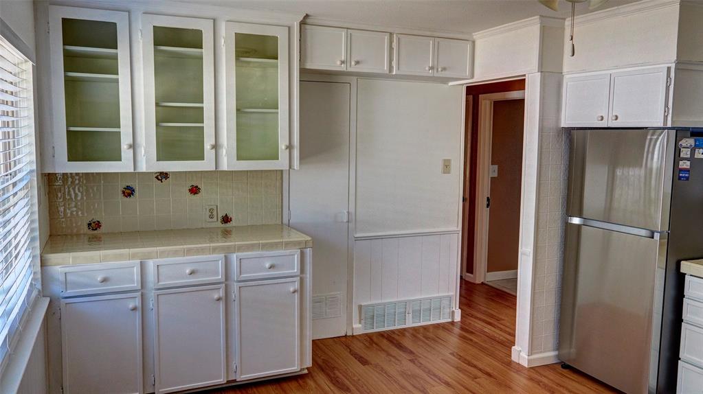 2612 West Rochelle Road Irving, TX 75062 - Photo 15 of 29 Kitchen featuring white cabinetry, freestanding refrigerator, light wood-style flooring, glass insert cabinets, and light countertops