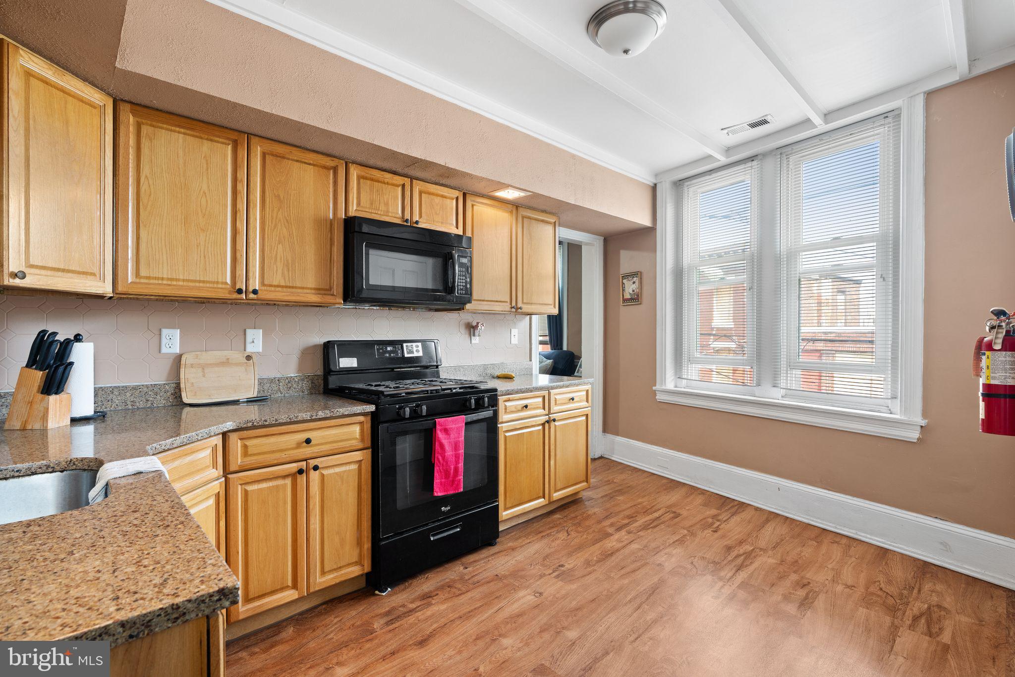 4600 Wayne Avenue Philadelphia, PA 19144 - Photo 17 of 25 a kitchen with granite countertop a stove top oven a sink dishwasher and wooden cabinets with wooden floor