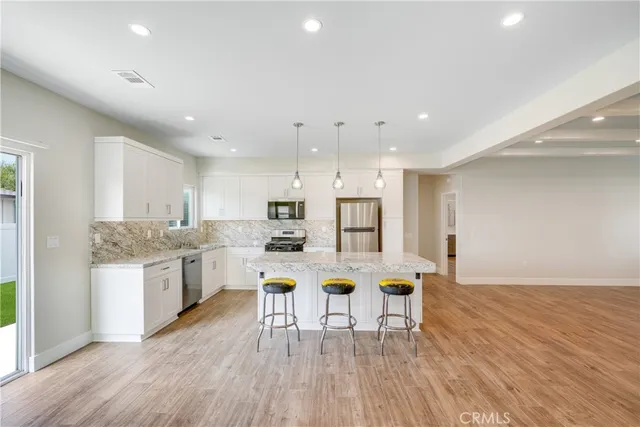 a dining hall with stainless steel appliances granite countertop a stove top oven a dining table and chairs with wooden floor