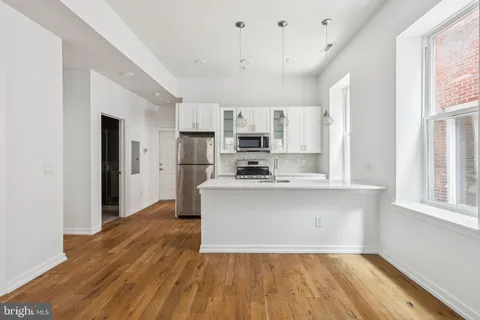 a kitchen with stainless steel appliances granite countertop a refrigerator a stove a sink and white cabinets with wooden floor