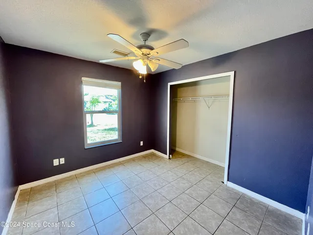 a view of an empty room with window and chandelier fan