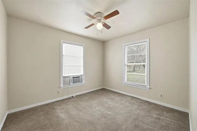 an empty room with chandelier fan and windows