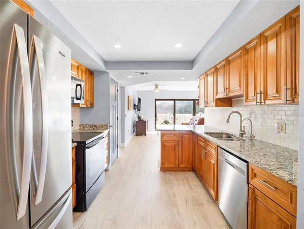 a large kitchen with stainless steel appliances granite countertop a refrigerator a sink dishwasher a stove and white countertops with wooden floor