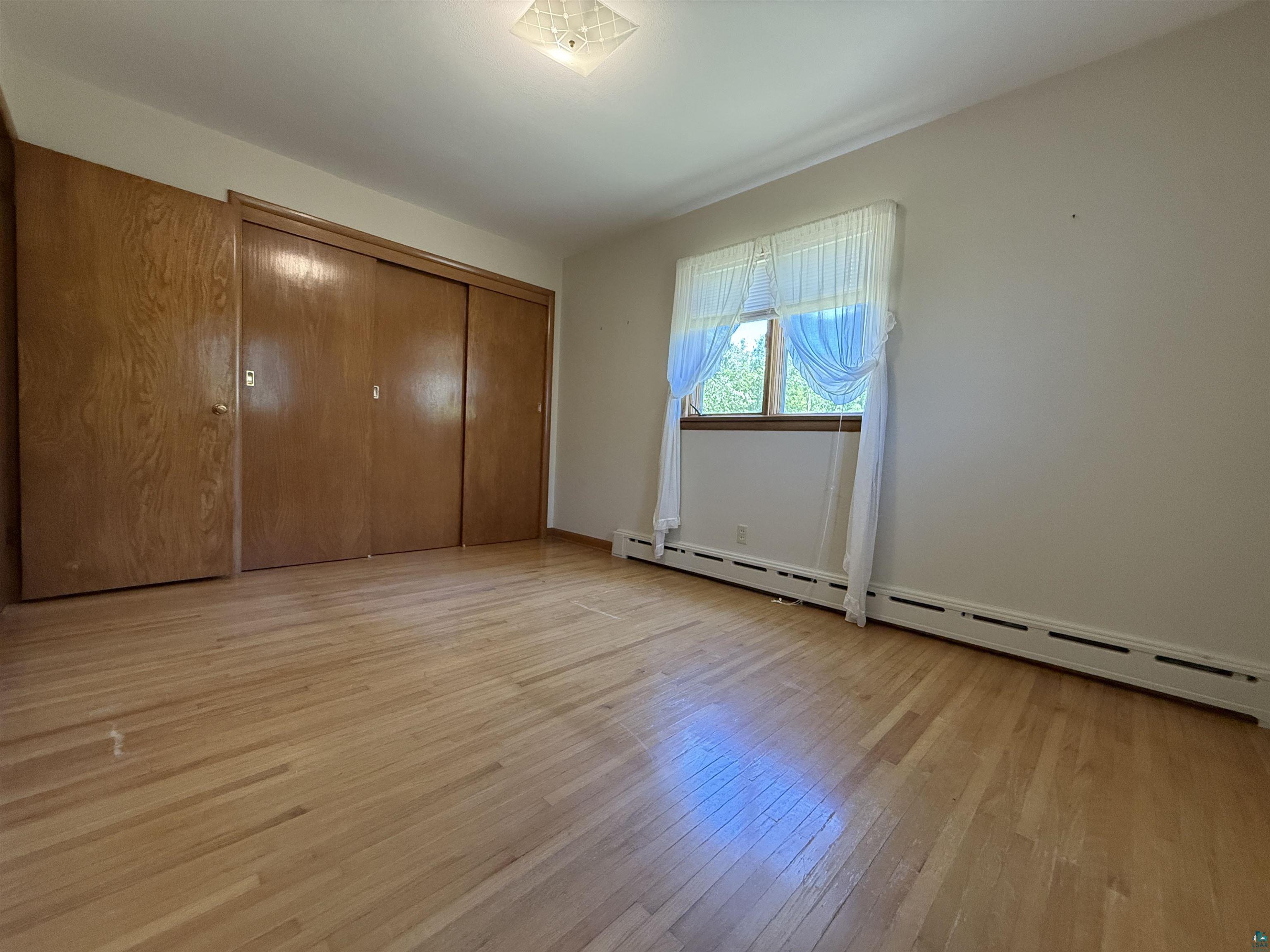 607 3rd Street Northeast Chisholm, MN 55719 - Photo 16 of 32 Bedroom featuring wood-finish flooring, a window with natural light, and two large closet doors
