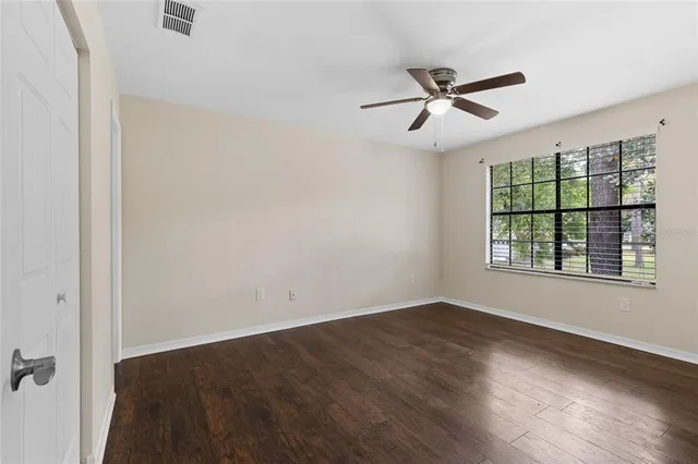 an empty room with wooden floor ceiling fan and windows