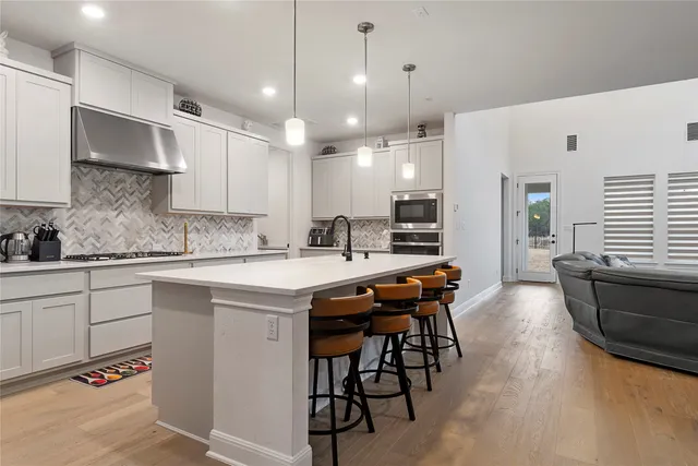 a kitchen with stainless steel appliances granite countertop a sink a stove a refrigerator and island with wooden floor