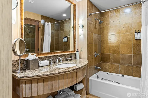 a bathroom with a granite countertop sink a mirror a bathtub and shower