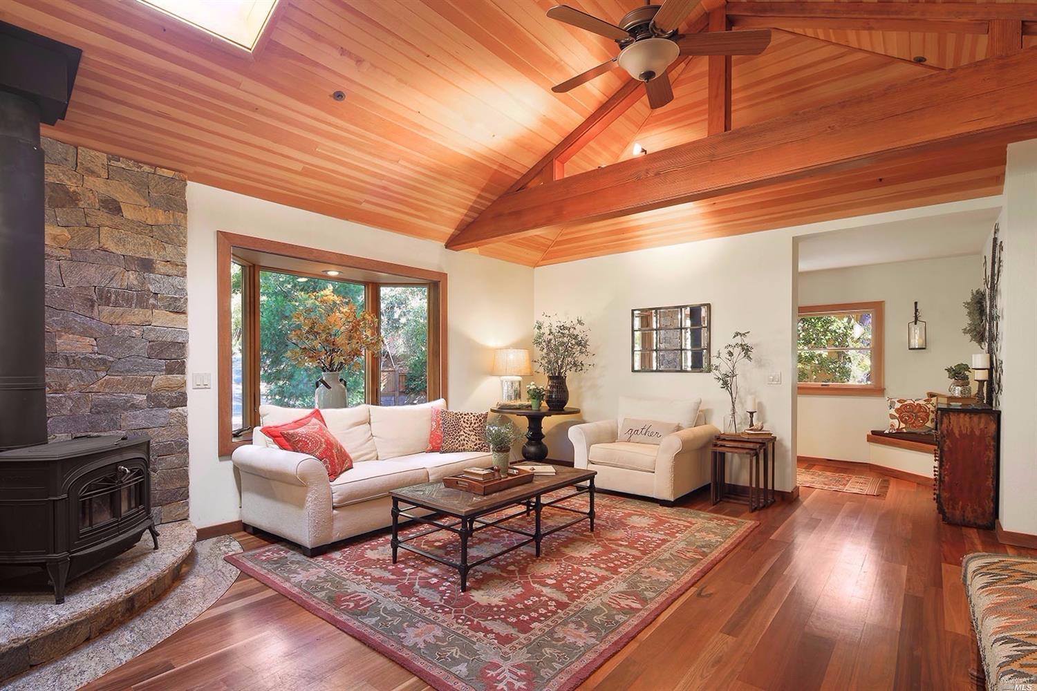 Living room with vaulted ceilings, remote control air redistributor fan, Australian Spotted-Gum hardwood floors, bay window and Vermont Castings free standing fireplace