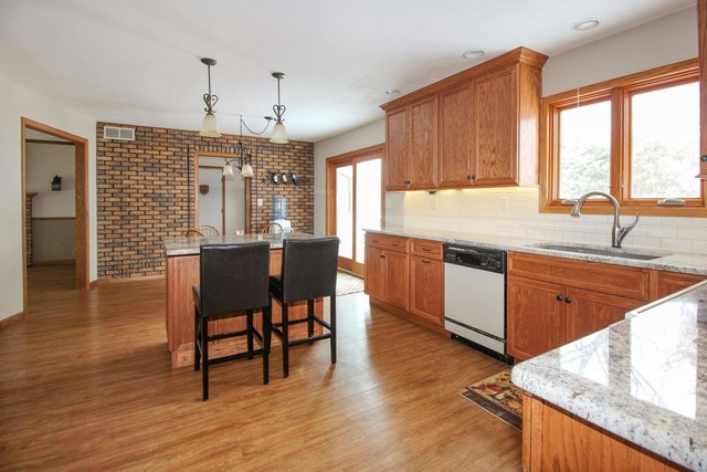 7417 East Maize Road Ridott, IL 61067 - Photo 12 of 46 a kitchen with granite countertop a sink dishwasher a stove a dining table and chairs with wooden floor