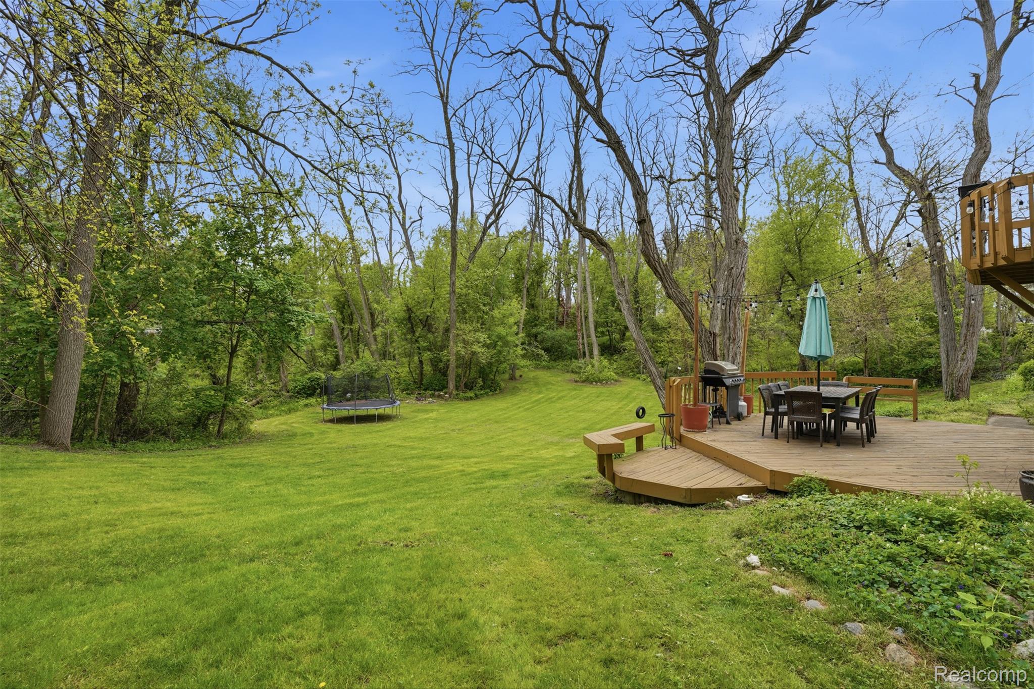 47129 Dunsany Road Northville, MI 48167 - Photo 39 of 49 View of grassy yard featuring outdoor dining space, a trampoline, and a wooden deck