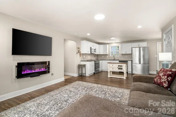 a living room with stainless steel appliances furniture a fireplace a flat screen tv and view kitchen