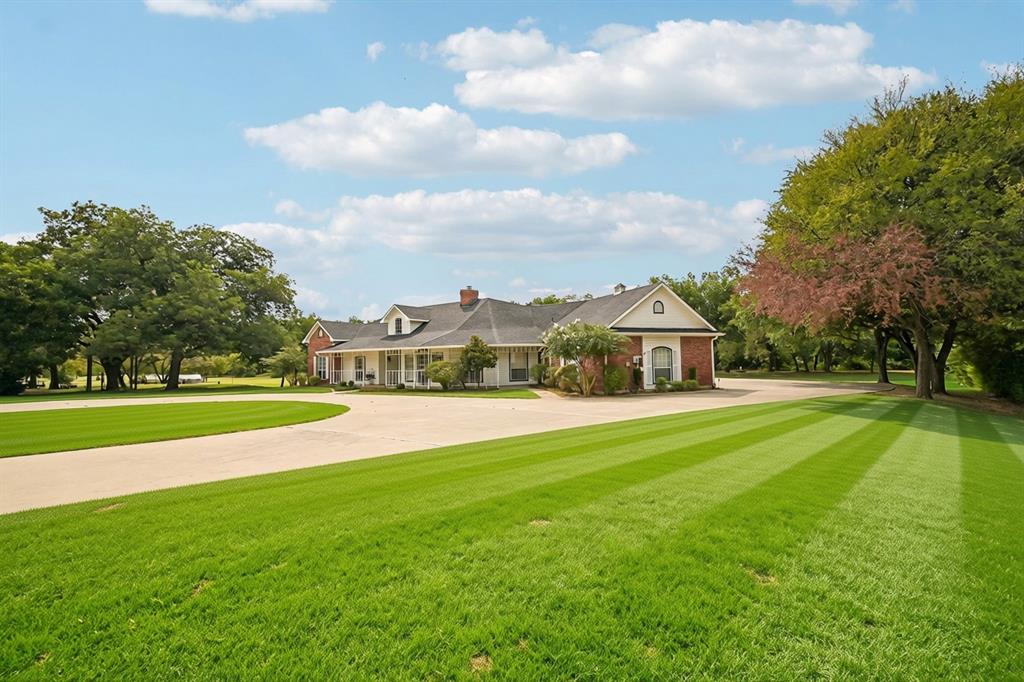 Expansive green lawn with striped patterns, mature trees, and a curved paved driveway leading to the residence