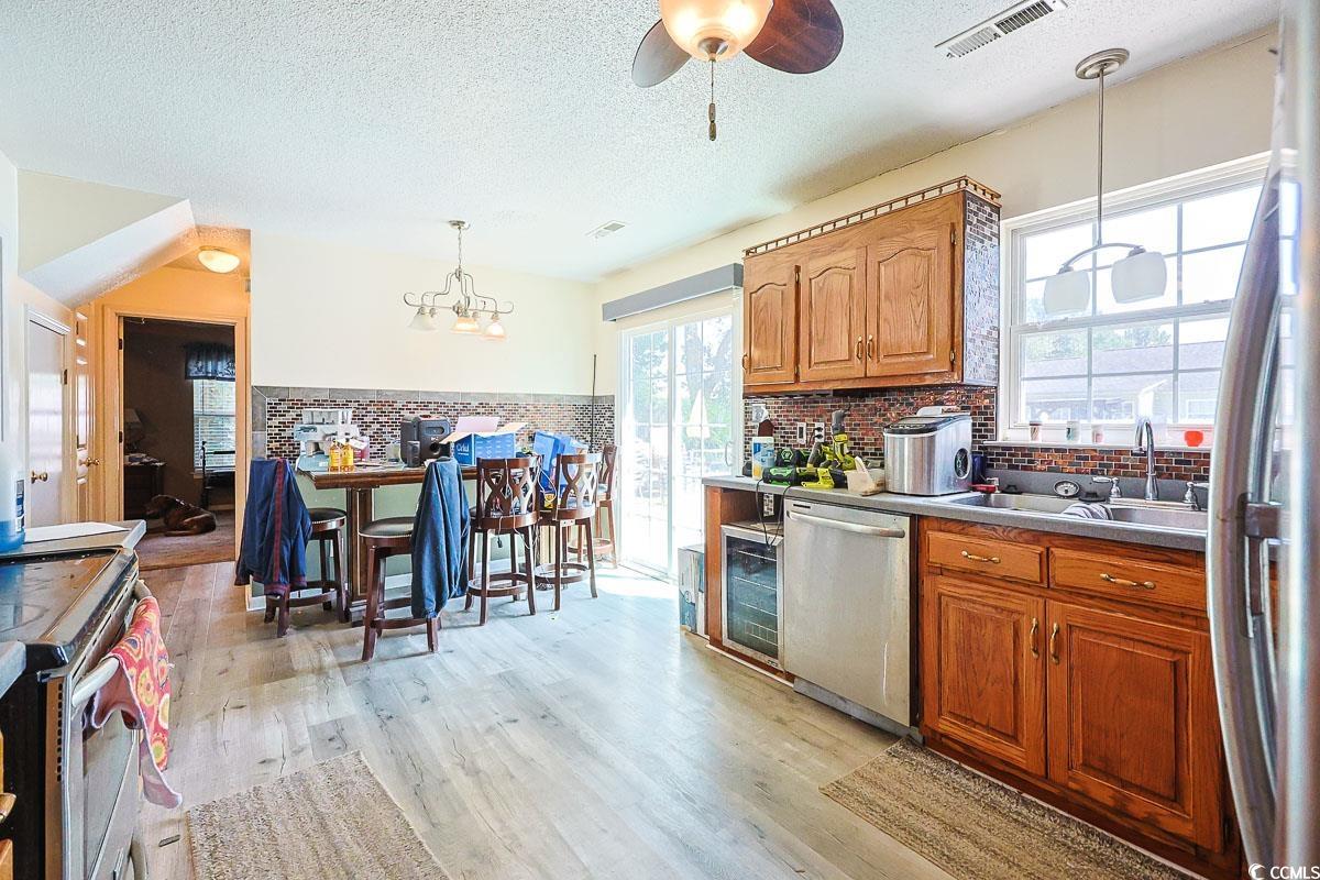 210 Rail Street Longs, SC 29568 - Photo 12 of 32 Kitchen featuring brown cabinets, a textured ceiling, appliances with stainless steel finishes, light wood finished floors, and a chandelier