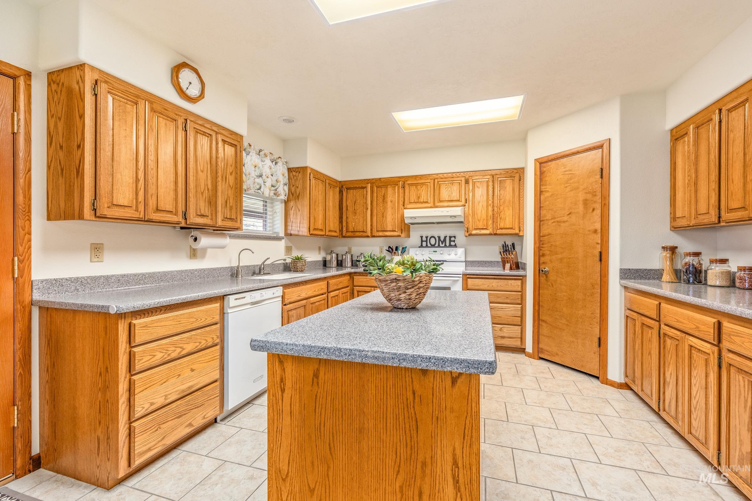 10514 Airpark Loop Road Melba, ID 83641 - Photo 20 of 47 Kitchen featuring white appliances, a kitchen island, wood finish cabinets, a skylight, and light stone counters