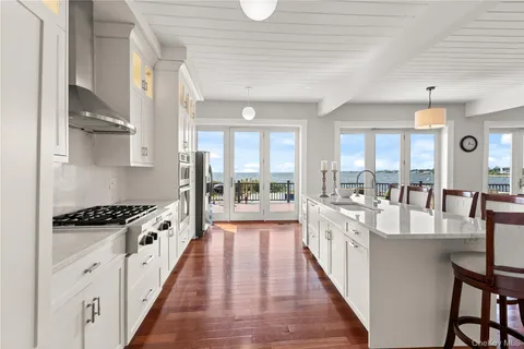 a kitchen with stainless steel appliances a stove top oven a sink a dining table and chairs with wooden floor