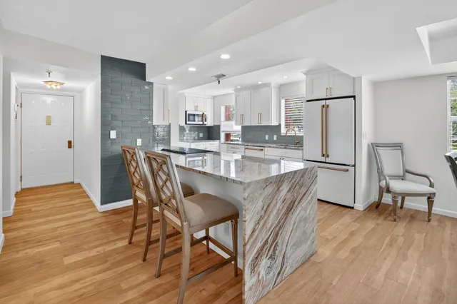 a kitchen with stainless steel appliances granite countertop a dining table chairs refrigerator and sink