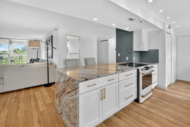 a kitchen with kitchen island granite countertop a stove a sink and white cabinets with wooden floor