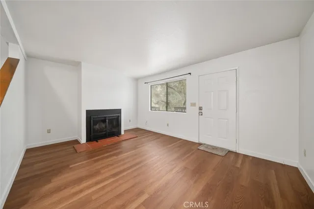 an empty room with wooden floor fireplace and windows