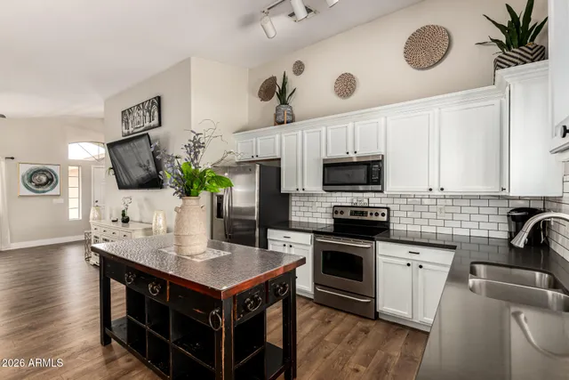 a kitchen with stainless steel appliances a stove a sink a microwave a refrigerator a stove and white cabinets with wooden floor