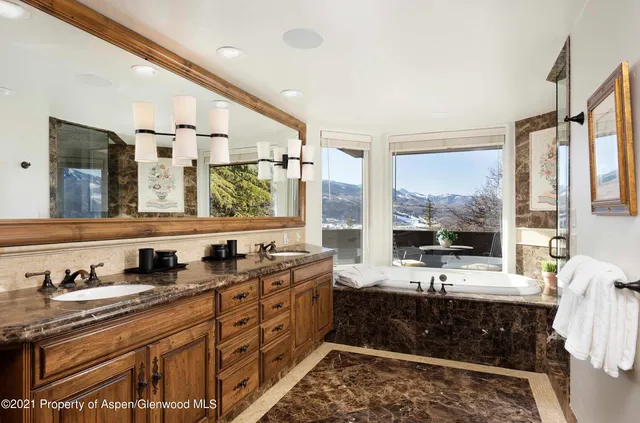 a bathroom with double vanity sinks a large mirror and a bathtub next to a window